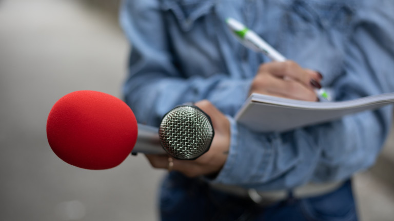 Journalist at news conference, writing notes, holding microphones