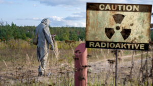 Military dosimetrist measures the radiation area, a sign with the inscription: caution, radiation, chemical protective suit and gas mask